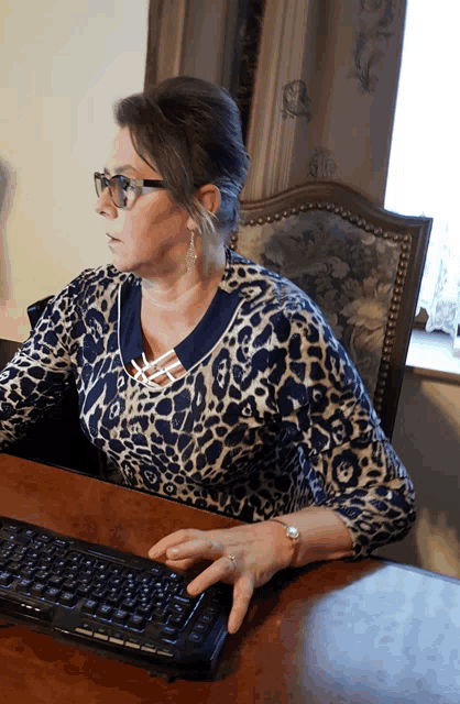 a woman in a leopard print shirt sits at a desk using a keyboard