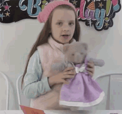 a little girl in a pink hat is holding a teddy bear