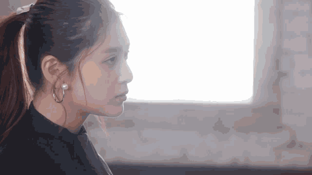 a woman with a ponytail and hoop earrings looks to the side