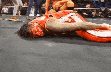 a man is laying on the ground in a wrestling ring with blood on his face .