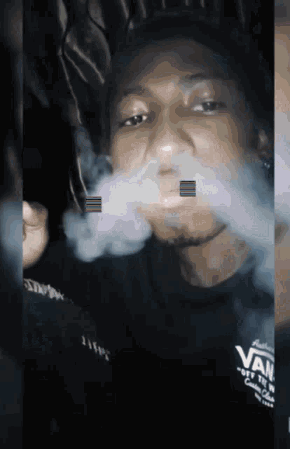 a man wearing a vans off the wall shirt smoking a cigarette