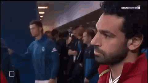 a man in a red jacket is standing in front of a group of people in a locker room .
