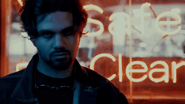 a man standing in front of a neon sign that says safe clear