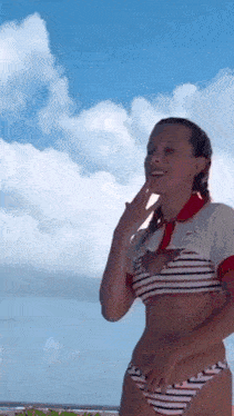 a woman in a striped bikini is standing on a beach with a blue sky in the background .