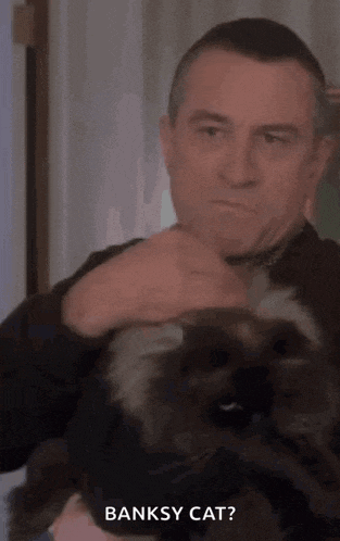 a man is holding a cat in his arms and the cat is saying banksy cat ?
