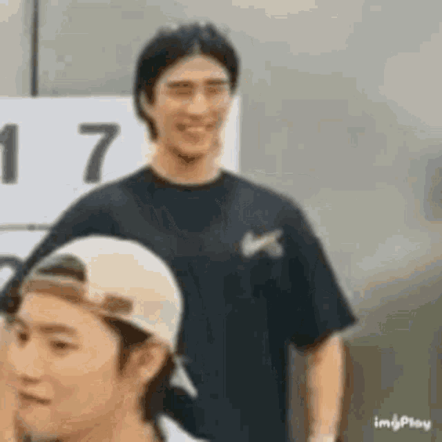 a man wearing a baseball cap is standing next to another man wearing a black shirt .
