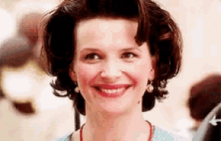 a woman wearing a blue sweater and a red necklace smiles for the camera