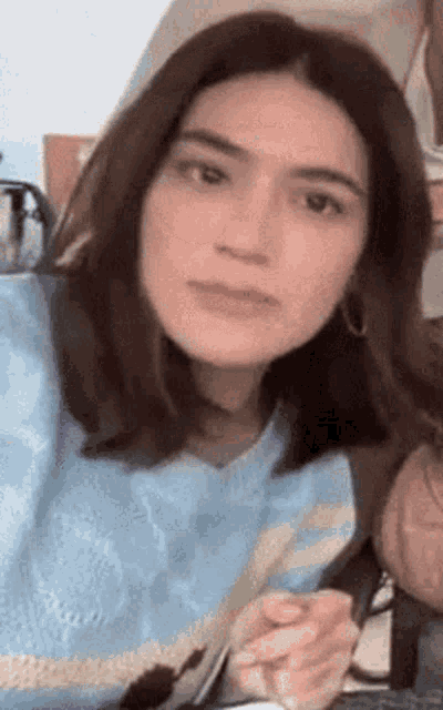 a woman in a blue sweater is sitting at a table eating food with a fork .