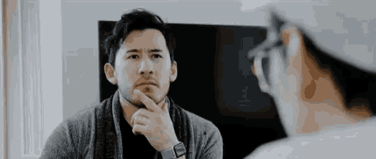 a man with a beard is looking at himself in the mirror while wearing glasses .