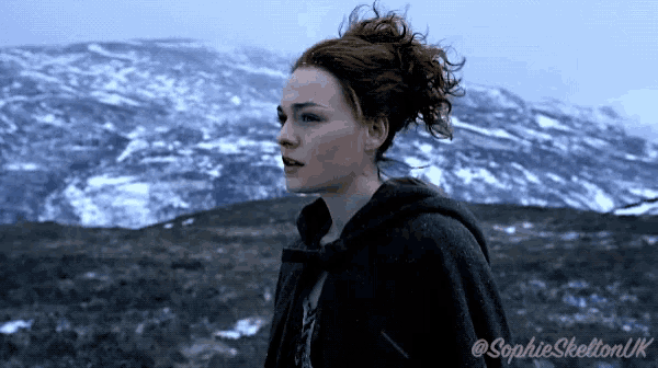 a woman in a cape stands in front of a snowy mountain with the name sophie skelton uk below her