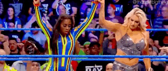 a couple of women are standing in a wrestling ring with their hands in the air .