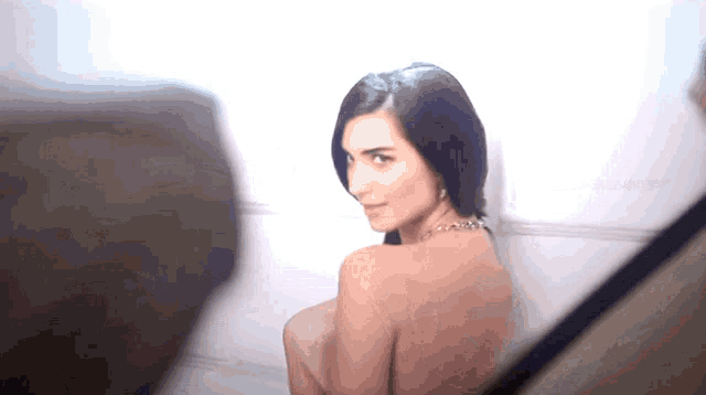 a woman without a shirt is standing in front of a wall