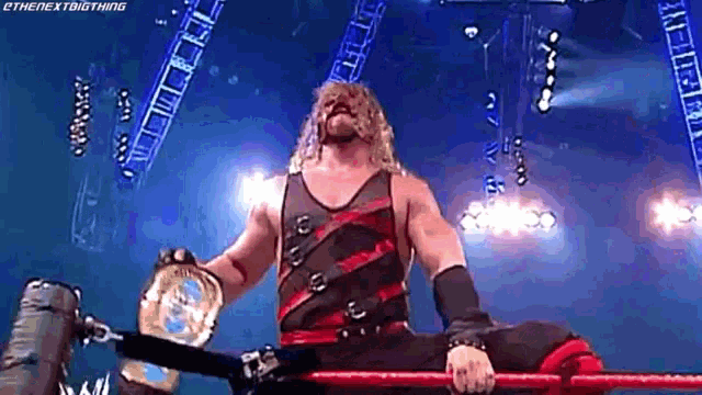 a wrestler is holding a world heavyweight championship while sitting on a rope in a wrestling ring .