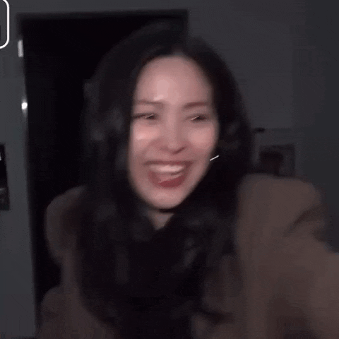 a woman in a brown coat is standing in a dark room and making a funny face .