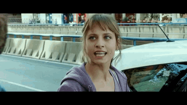 a woman in a purple sweatshirt is standing in front of a car