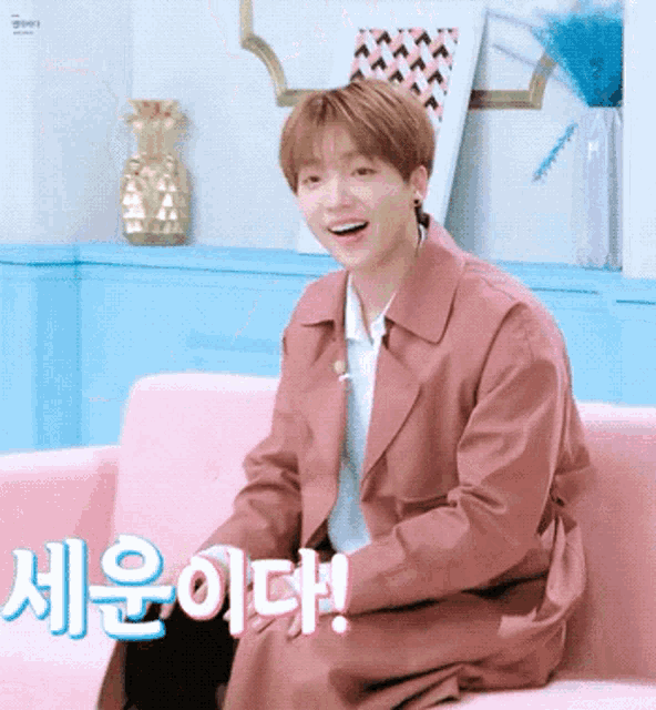 a young man in a pink trench coat is sitting on a pink couch and smiling .