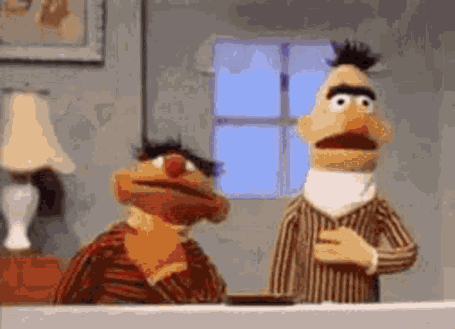ernie and bert from sesame street are standing next to each other in a room .