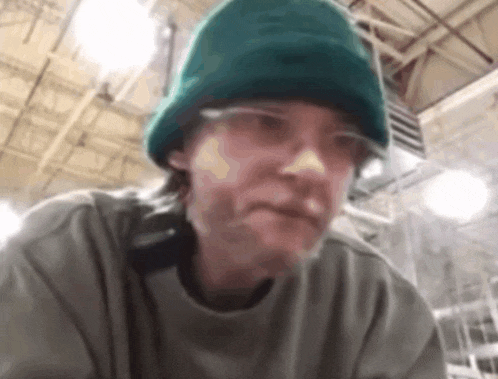 a man wearing a green hat and glasses is sitting in a room .