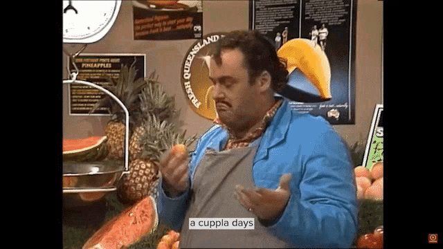 a man standing in front of a fruit stand with a sign that says fresh queensland on it