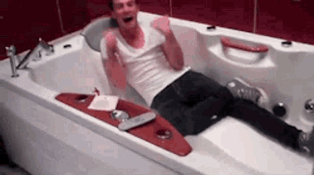 a man in a white shirt is laying in a bathtub with his arms in the air .