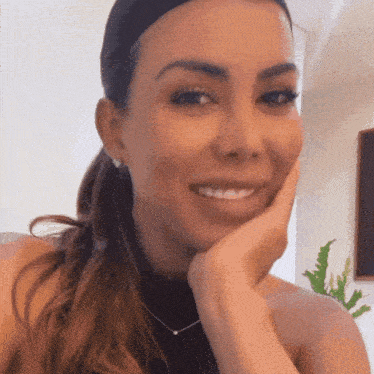 a woman wearing earrings and a necklace smiles with her hand on her chin
