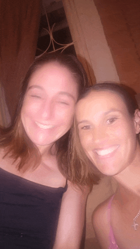 two women are posing for a picture and one has a necklace with a butterfly on it