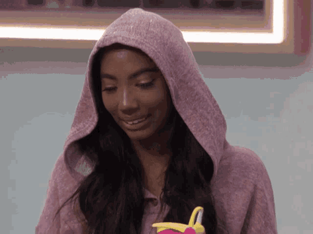 a woman wearing a pink hoodie is holding a yellow toy