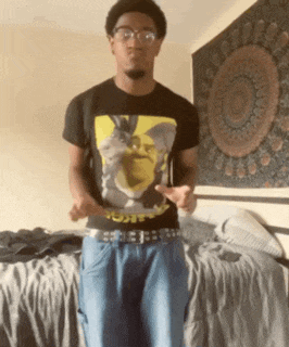 a man wearing a shrek t-shirt and glasses is standing in front of a bed