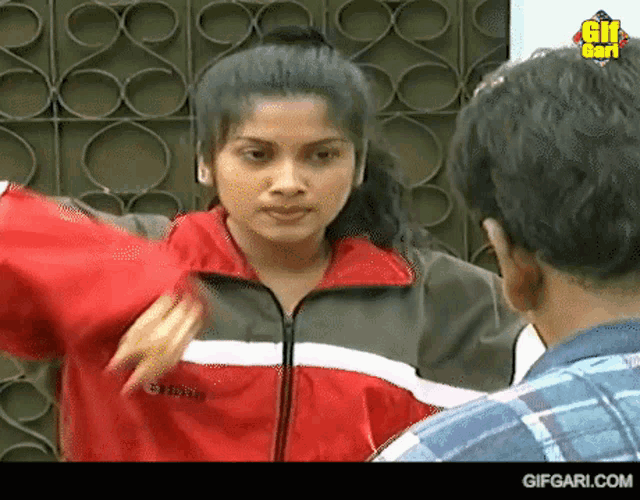 a woman in a red and grey jacket is talking to a man in a plaid shirt