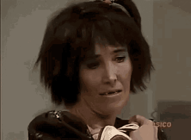 a woman with short hair is holding a pair of shoes and making a face .