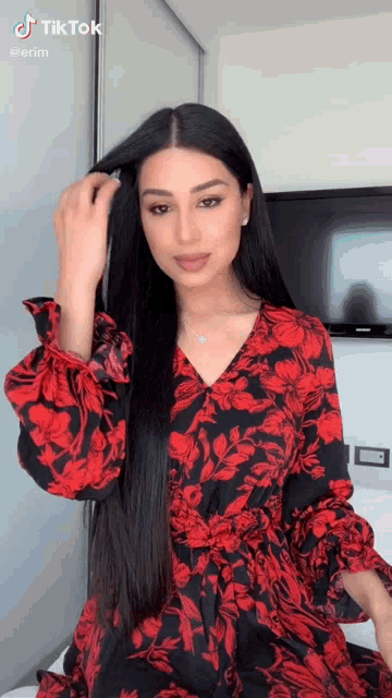 a woman in a red and black floral dress is standing in front of a tv .