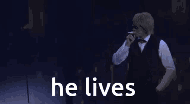 a man in a tuxedo is smoking a cigarette while standing on a stage .