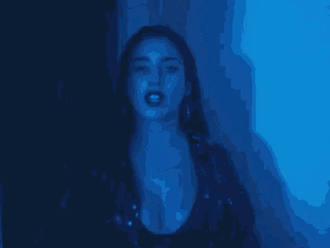 a woman in a black leather jacket is standing in a dark room with a blue light behind her .