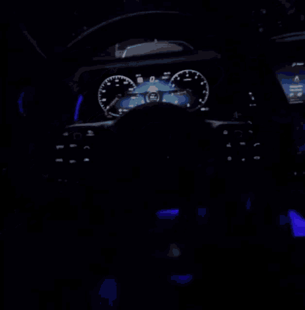 a blurry picture of a car dashboard with a blue light behind the steering wheel