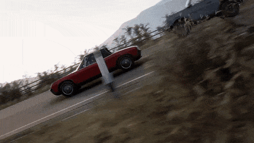 a red car is driving down a road with a person standing on the side of it