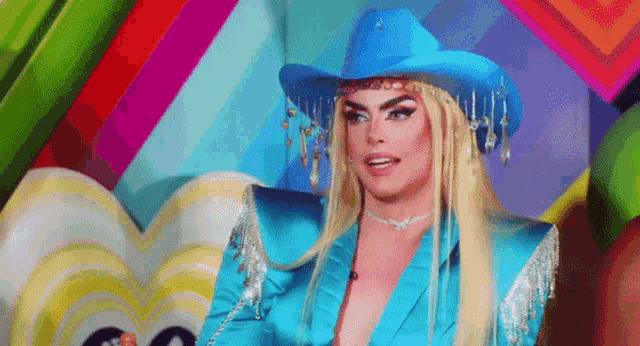 a drag queen is wearing a blue cowboy hat and blue jacket .