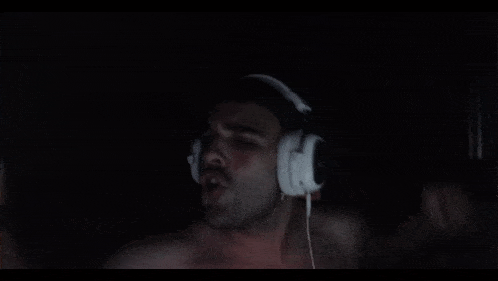 a man without a shirt is wearing white headphones in a dark room