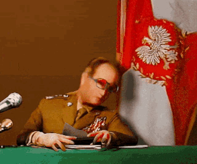 a man in a military uniform sits at a table with a microphone