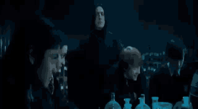 a group of people are sitting around a table with bottles of liquid in a dark room .