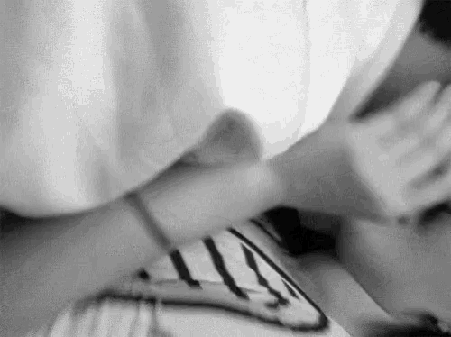 a black and white photo of a person laying on a bed with their hands on their face .