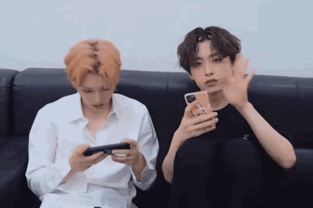 two young men sit on a couch looking at their phones