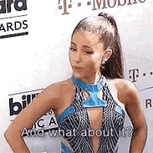 ariana grande is standing in front of a billboard with her hands on her hips and looking at the camera .