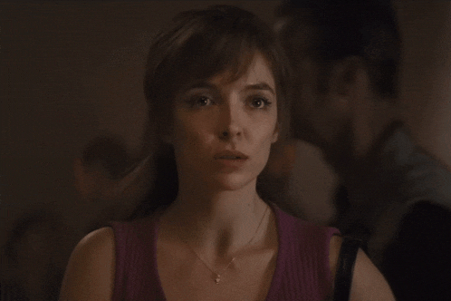 a woman wearing a purple tank top and a necklace looks at the camera