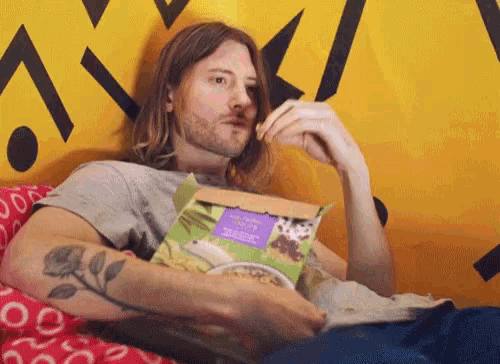 a man with a tattoo on his arm is eating cereal from a box