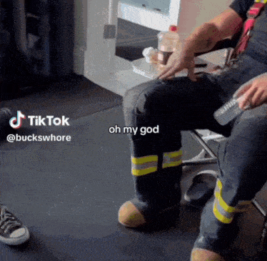 a fireman is sitting on a chair holding a remote control and a bottle of water