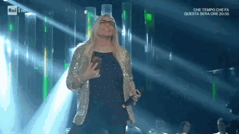 a woman singing into a microphone on a stage in front of rai