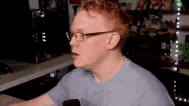 a man with red hair and glasses is sitting in front of a microphone .