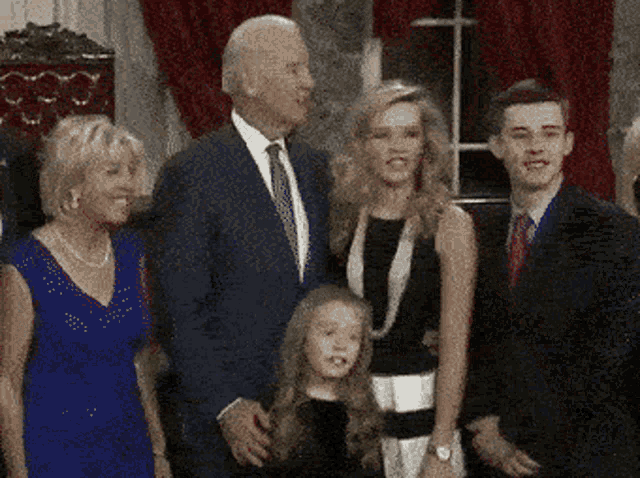 a man in a suit and tie stands next to a woman and two children