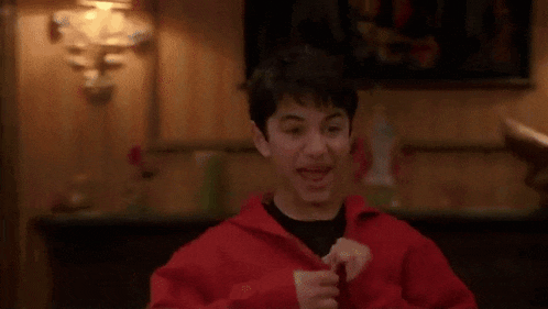 a young boy wearing a red jacket and a black shirt is standing in a living room .