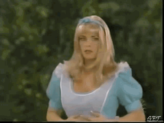 a woman dressed as alice from alice in wonderland is standing in a forest .
